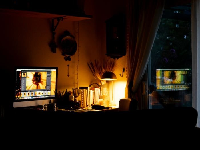 A dark room at night, lit only by a desk lamp and a glowing computer screen